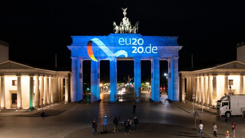 Brandenburger Tor bei Nacht mit angestrahltem Logo der Deutschen EU-Ratspräsidentschaft